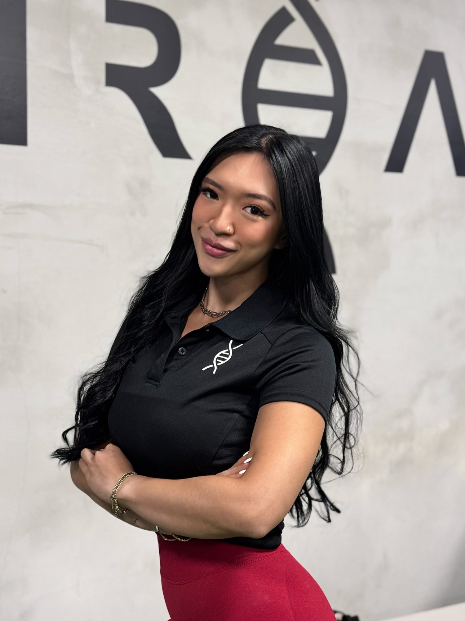 Unreal Personal Training's Advanced Trainer, Gloria Chung, in her black polo tee uniform with the UNREAL logo in the background